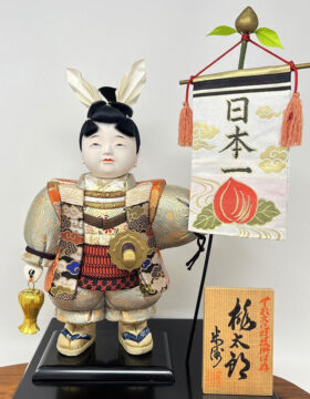 Esclusiva bambola giapponese “Momotarō” realizzata a mano con la pregiata tecnica kimekomi, con base e stendardo (33,5 cm)